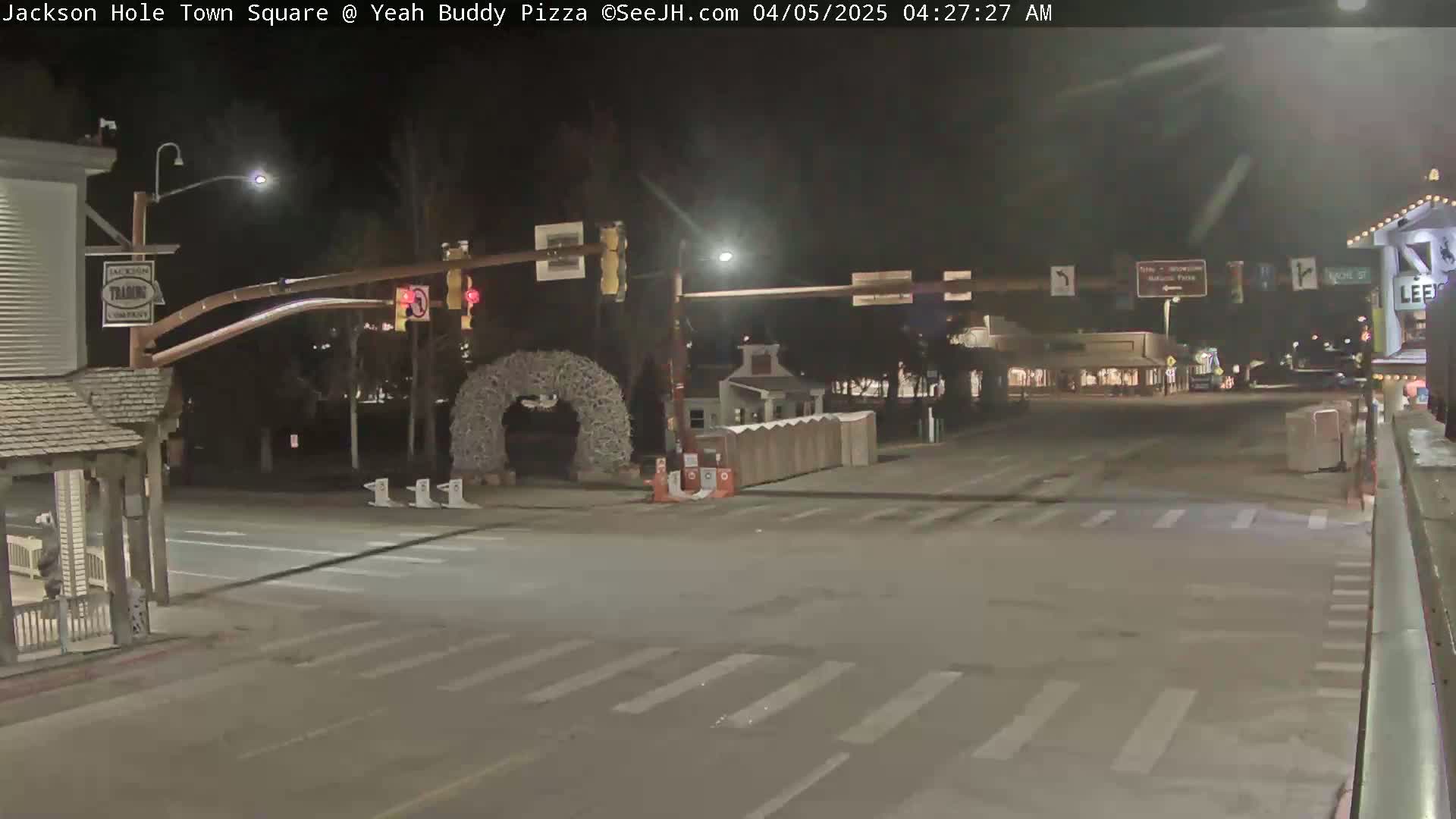 A nighttime, empty town square intersection shows a crosswalk, traffic signals, and a decorative archway.