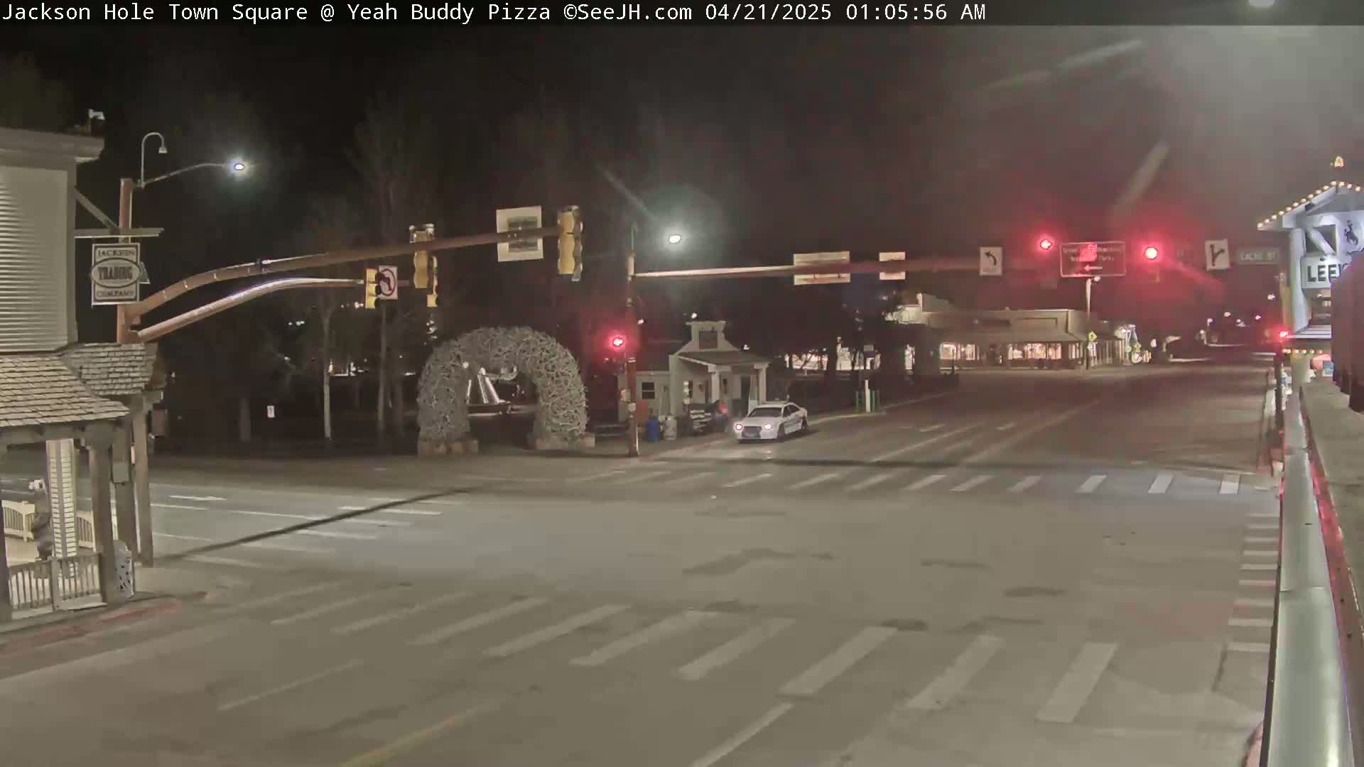 A nighttime view of a mostly empty town square intersection with a single car and traffic signals.