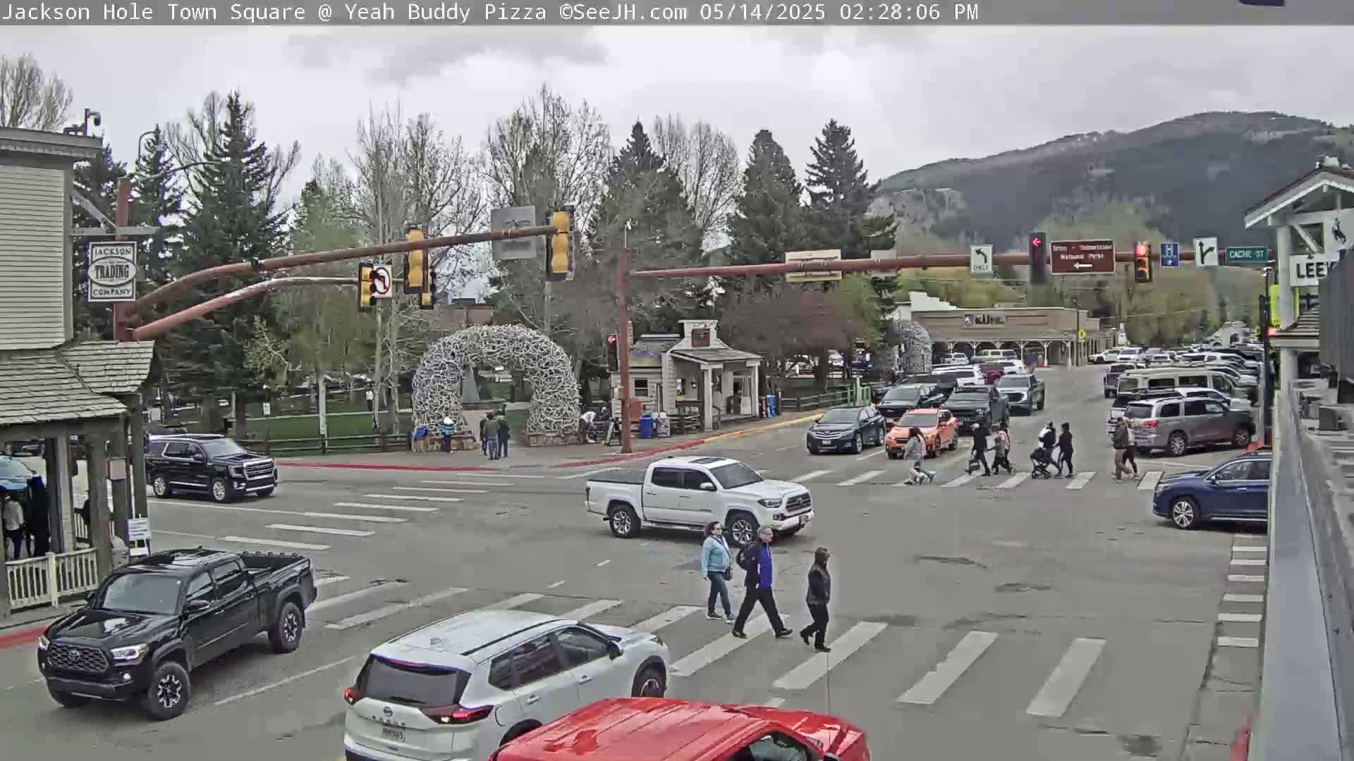 A town square intersection with several vehicles and pedestrians under an overcast sky.