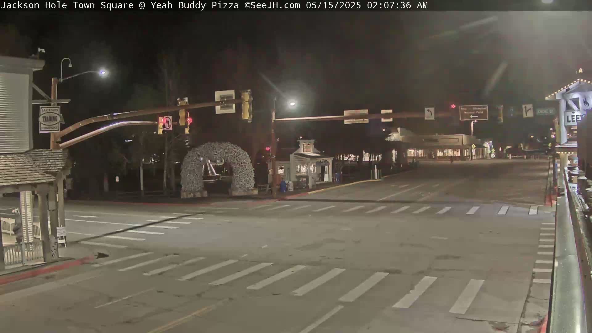 A nighttime, empty town square intersection with crosswalks, traffic lights, and a decorative archway.