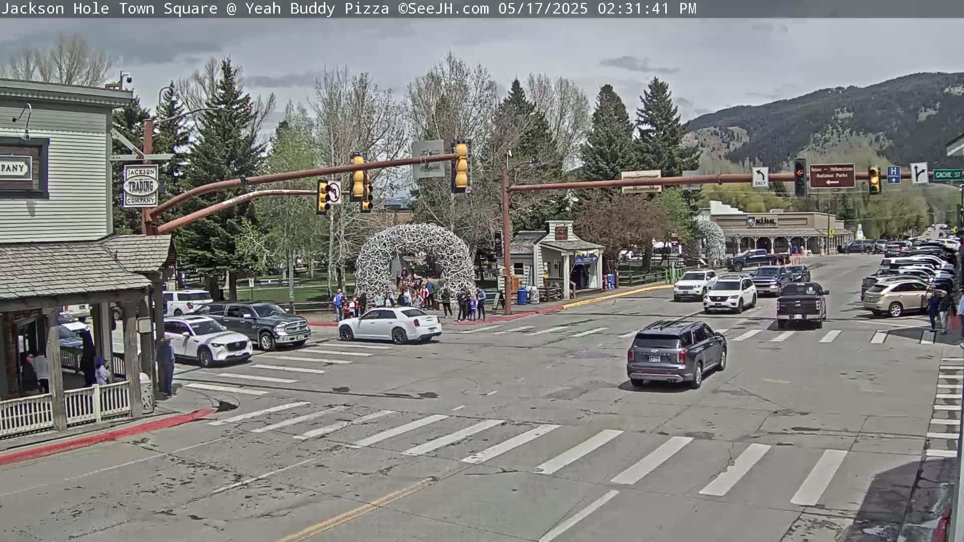 A town square with several cars at an intersection on a partly sunny day, with a large antler arch in the background.
