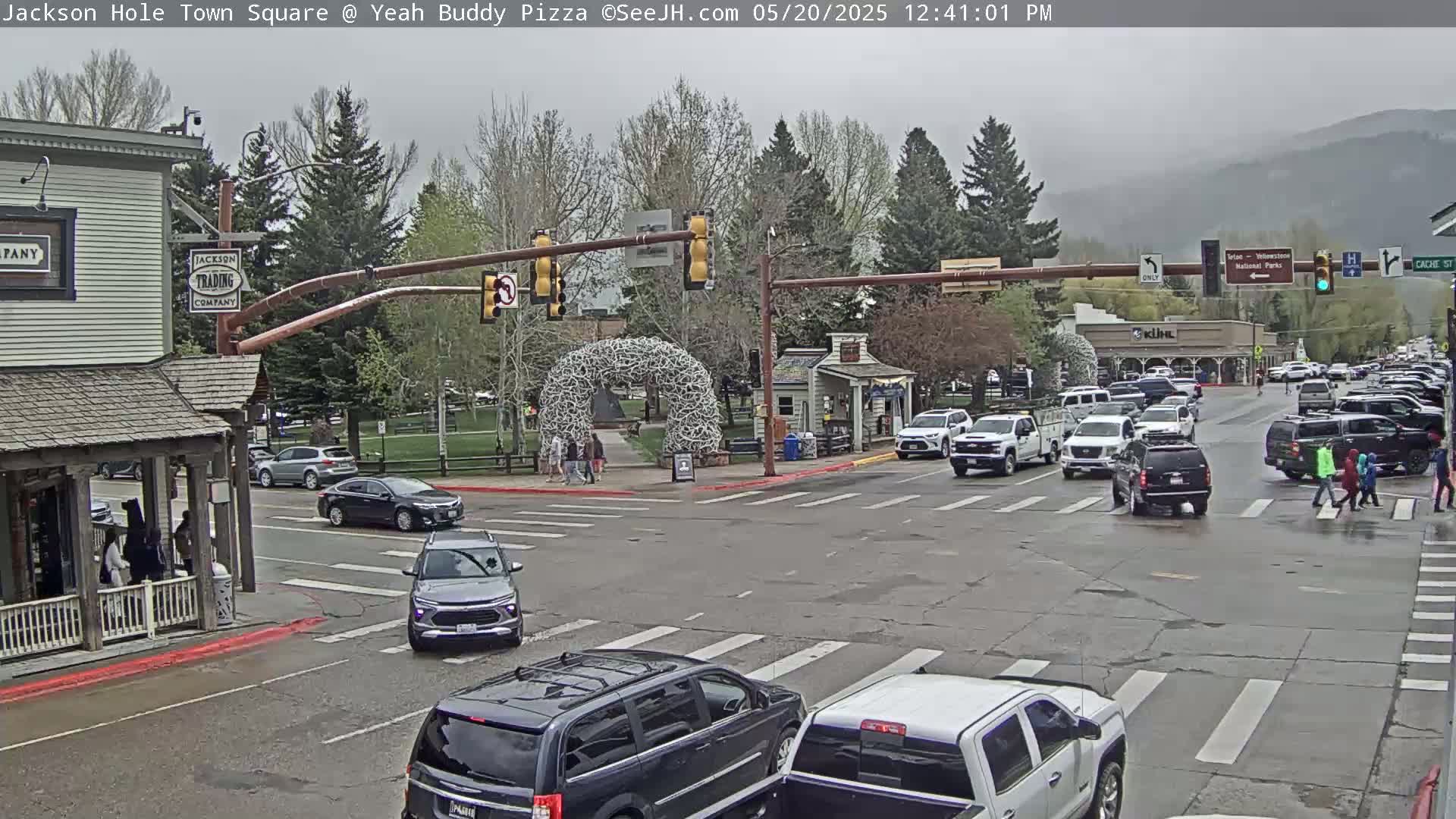 A town square intersection with several vehicles and pedestrians under an overcast sky.