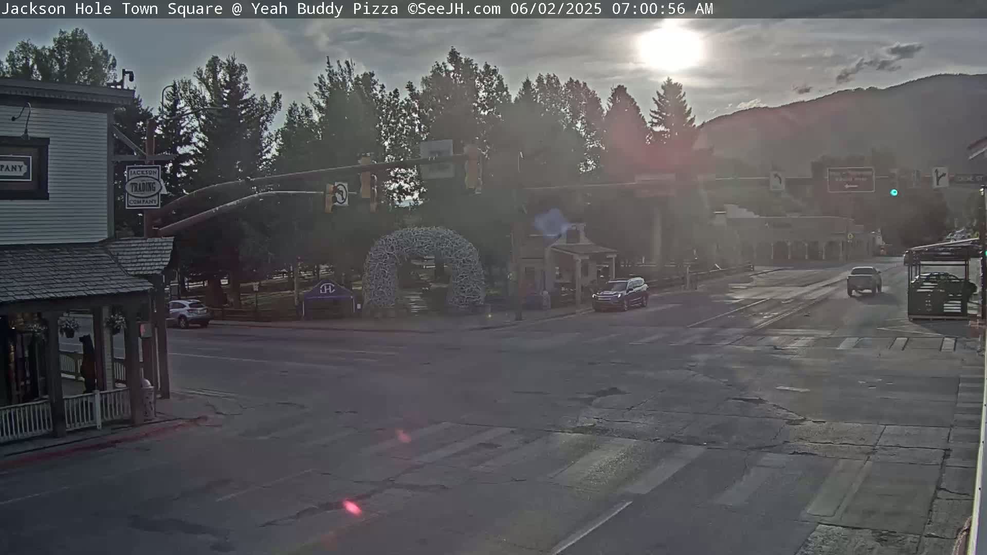 A town square intersection at sunrise, with a few vehicles present and a large antler arch in the center.
