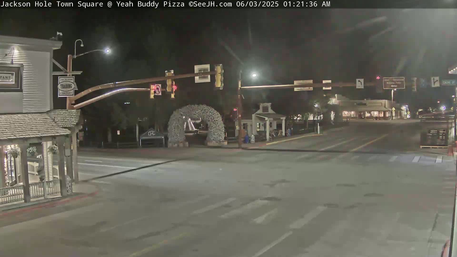 A nighttime view of a town square intersection with a large antler archway, streetlights, and buildings.