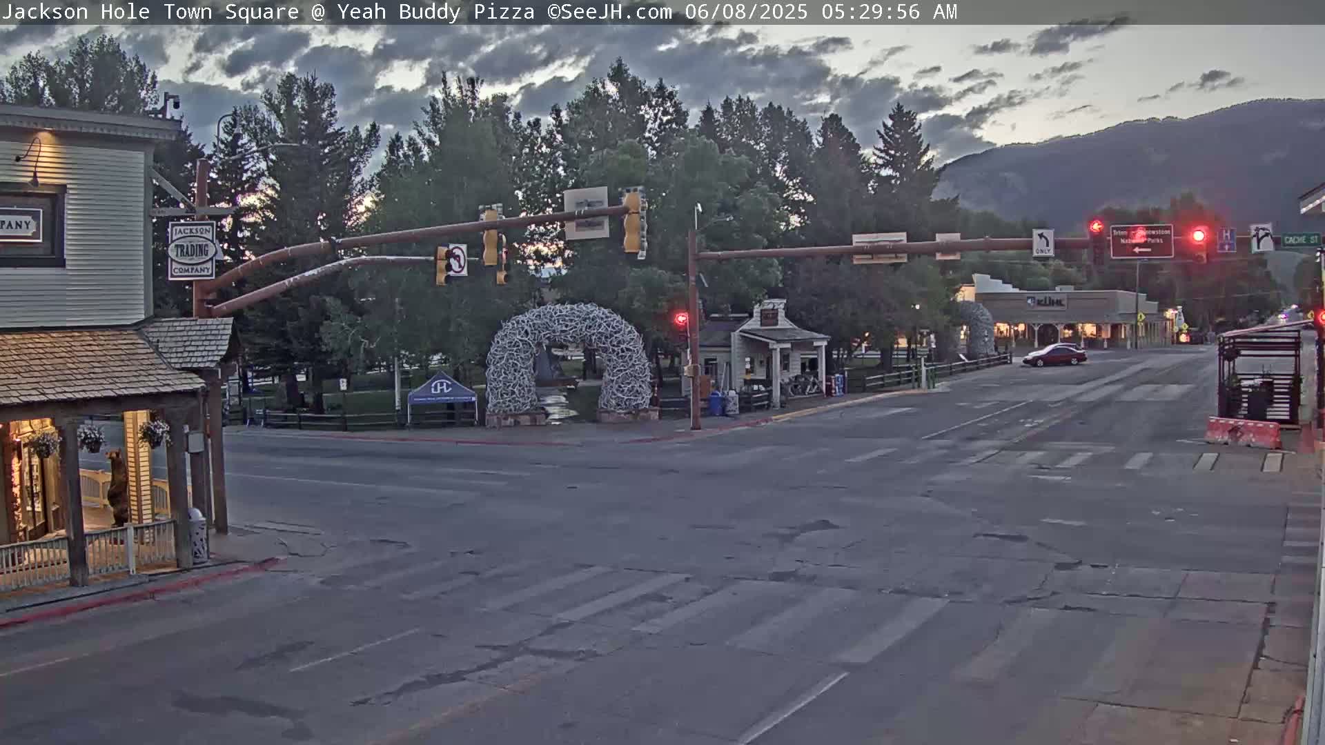 A mostly empty town square at dawn under a partly cloudy sky, with a large antler arch in the center and a single car on the road.