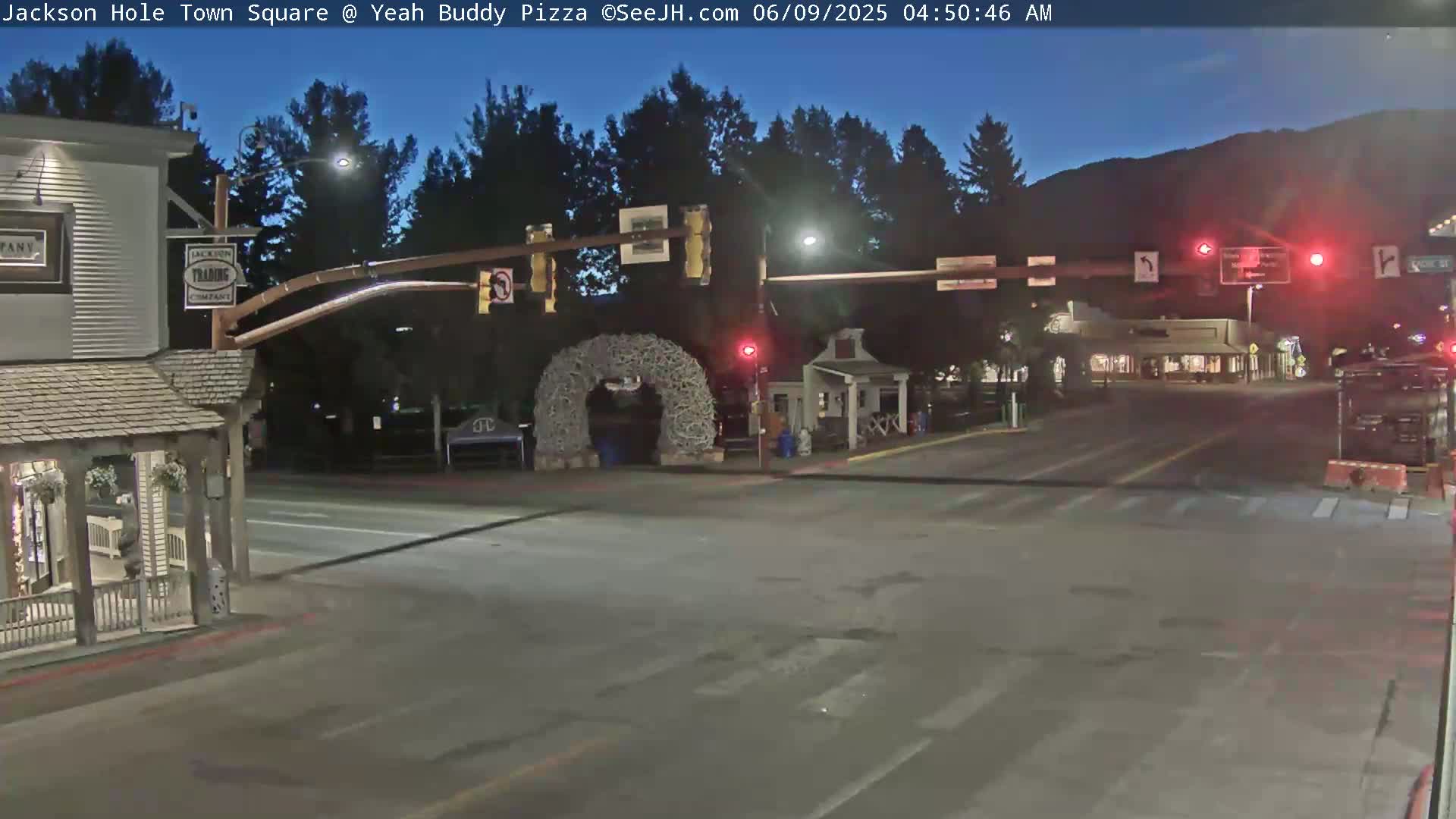 A mostly empty town square at night, under a twilight sky, with traffic lights and a large antler archway.