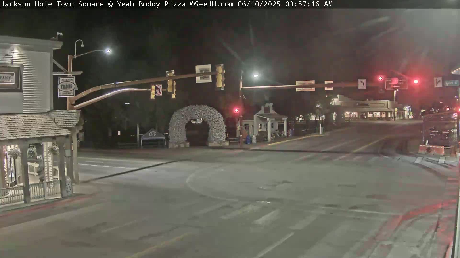 A nighttime view of a town square intersection with traffic lights, buildings, and a large antler archway.
