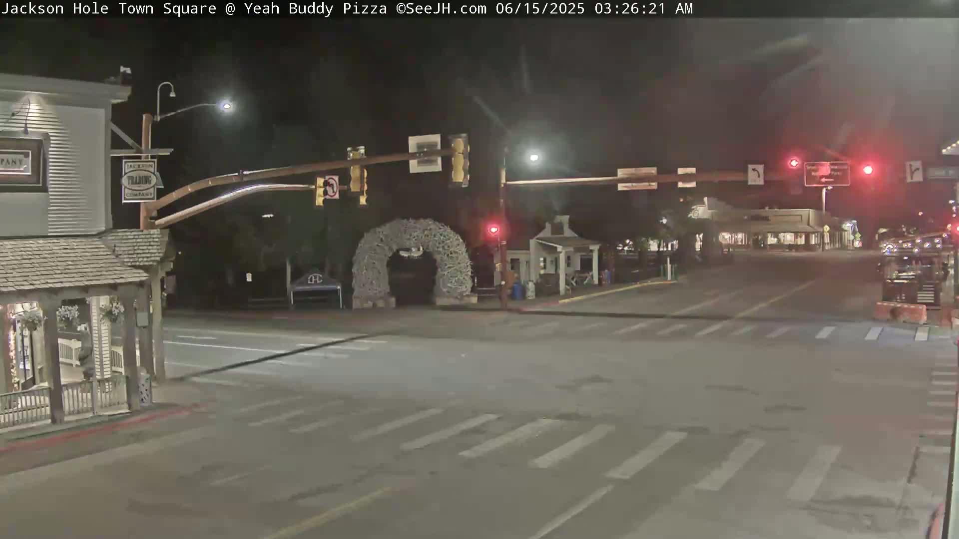 A nighttime view of a town square intersection with a large antler archway, traffic signals, and sparsely populated streets under clear skies.