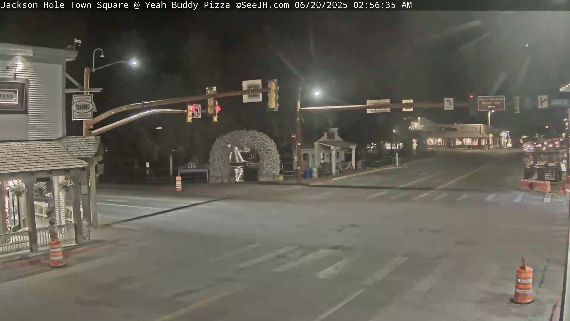 A nighttime view of a town square intersection with traffic lights, some buildings, and a large antler archway.
