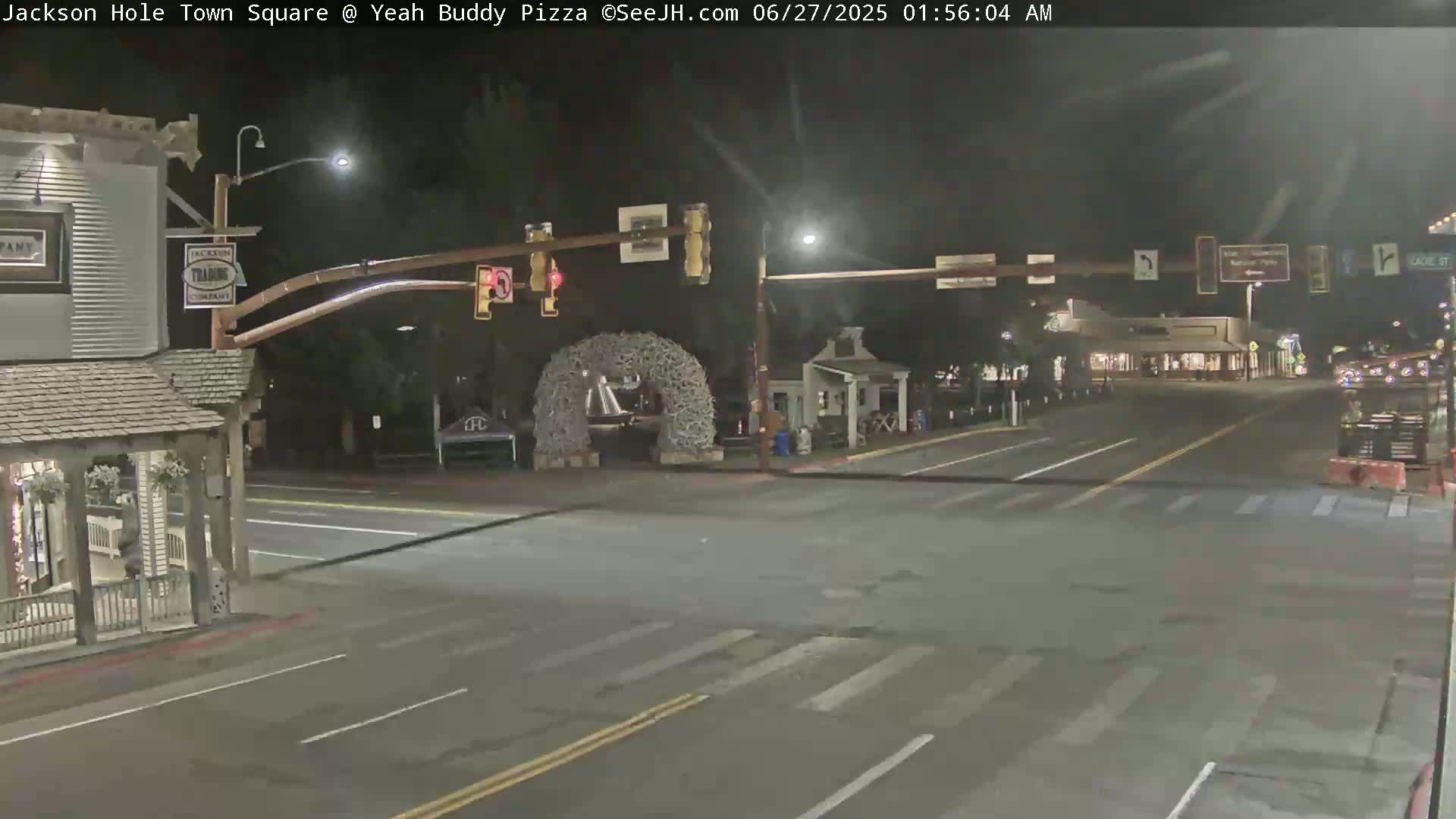 A nighttime view of a town square intersection with a traffic signal and a large antler archway, under clear skies.