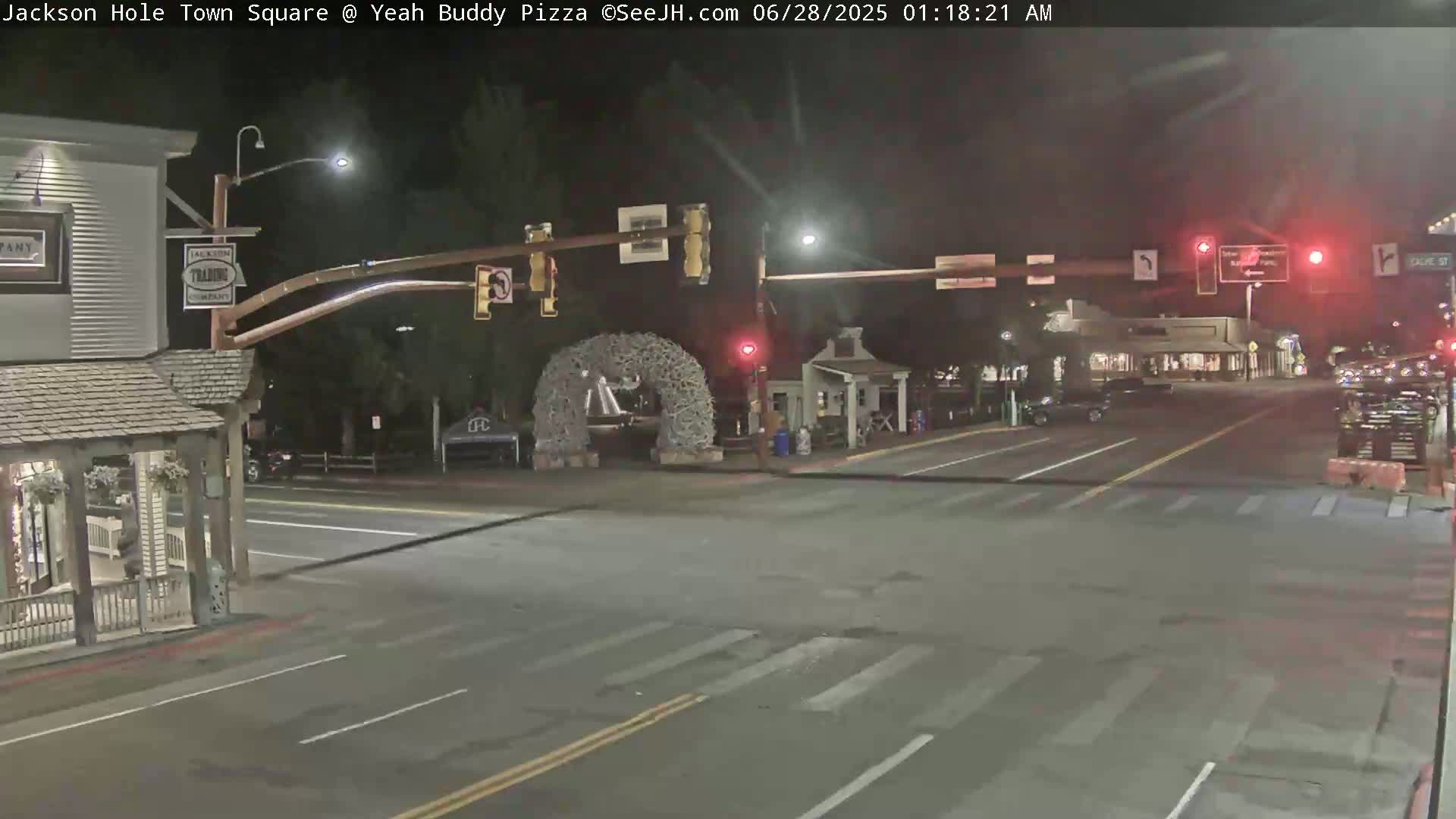 A nighttime street intersection with minimal traffic, featuring a large antler arch, and buildings lining the streets under dark conditions.