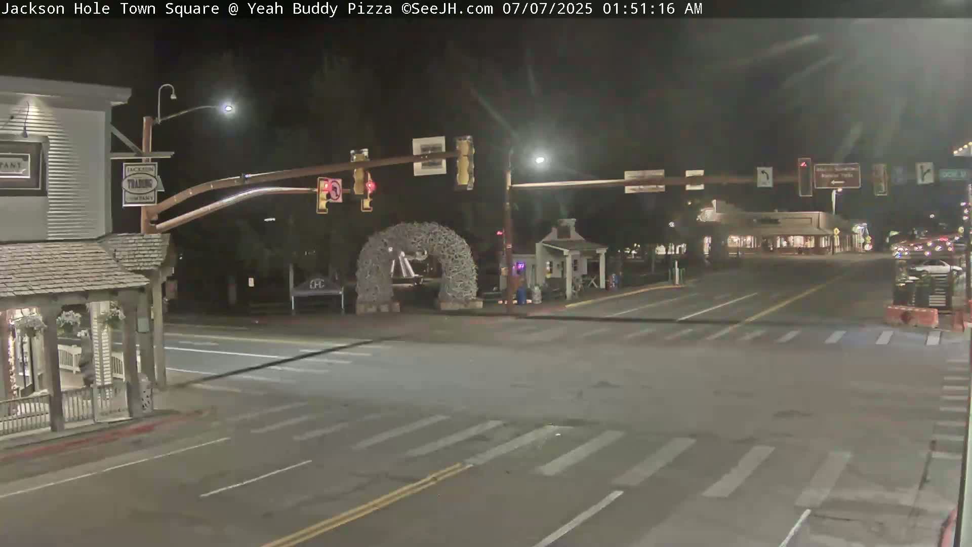A nighttime view of a town square intersection with traffic lights, buildings, and a large antler archway.