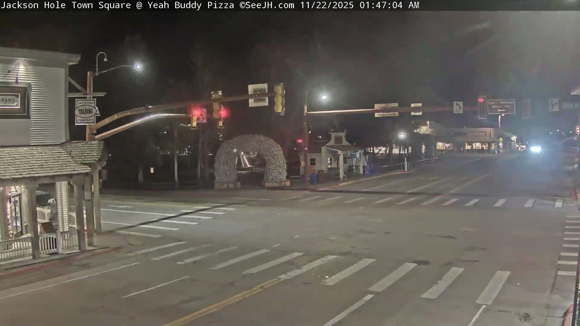 The image captures a quiet town square at night, illuminated by streetlights and featuring a large decorative archway in the center of an empty intersection, with clear weather conditions.