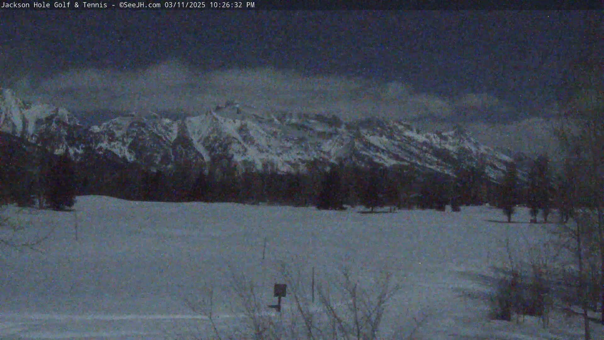 A snow-covered field stretches out before a range of snow-capped mountains under a twilight sky.