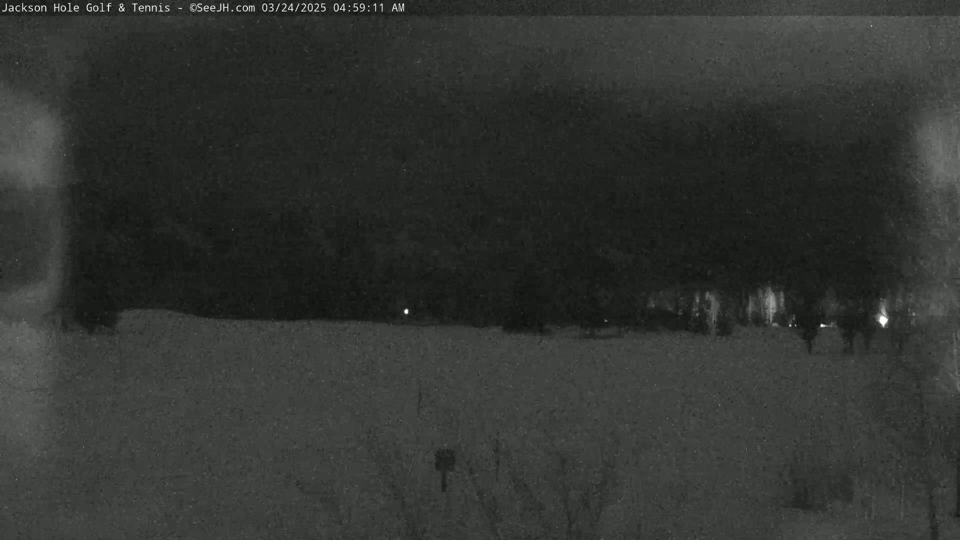 A nighttime, snow-covered landscape is visible, featuring dark trees in the background and a few faint lights.