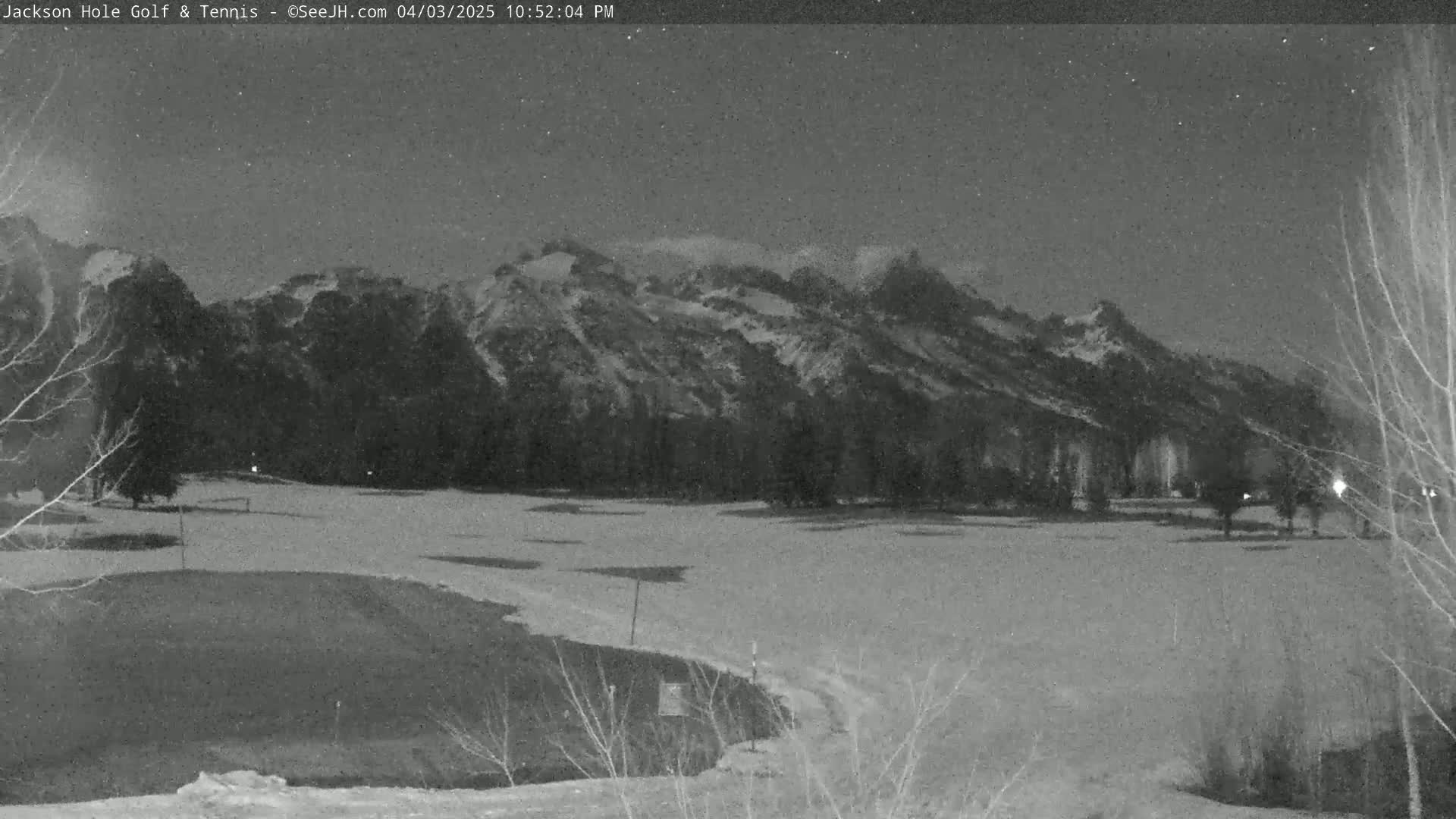 A snow-covered golf course at night, with a mountain range in the background under a mostly clear, starry sky.