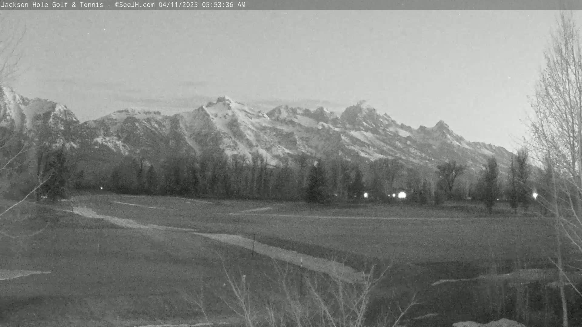 A snow-capped mountain range is visible in the background of a grayscale image showing a flat grassy field at dawn.