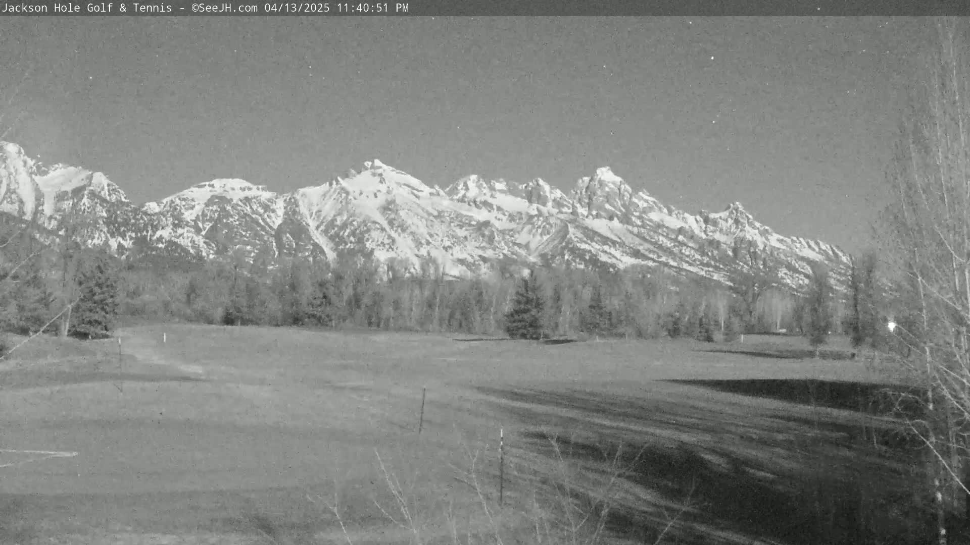 A snow-capped mountain range is visible in the background behind a flat, grassy field under a clear evening sky.