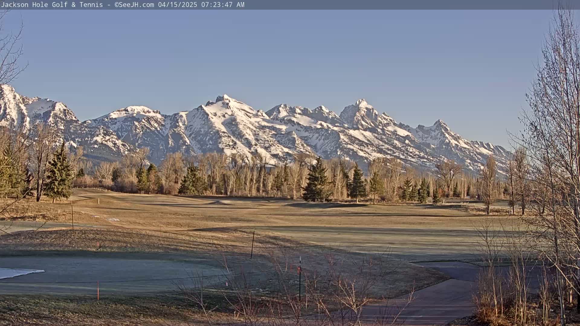 A snow-capped mountain range is visible in the background of a mostly barren golf course on a clear, sunny morning.