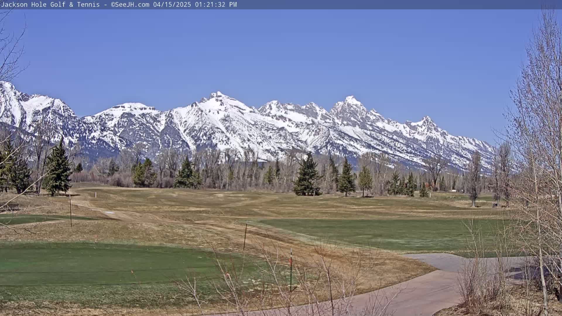 A snow-capped mountain range is visible in the background of a mostly barren golf course under a clear blue sky.