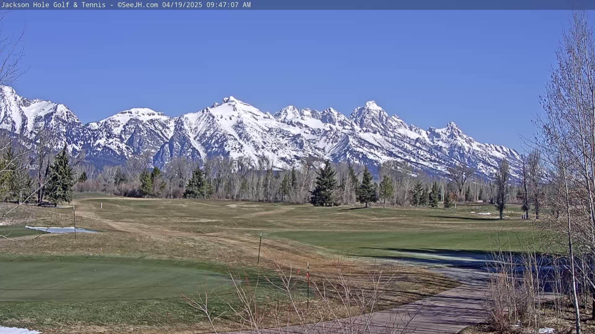A snow-capped mountain range is visible in the background of a golf course on a sunny day.