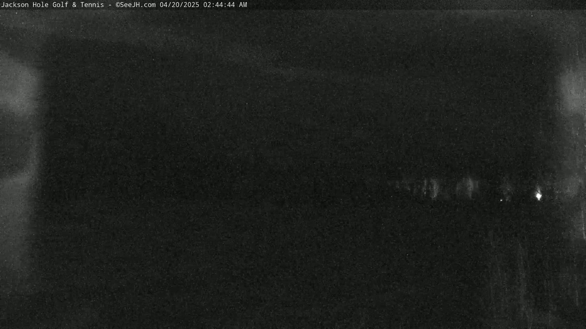 A low-light, nighttime image shows a dark, mostly featureless scene with a few faint lights visible in the distance.