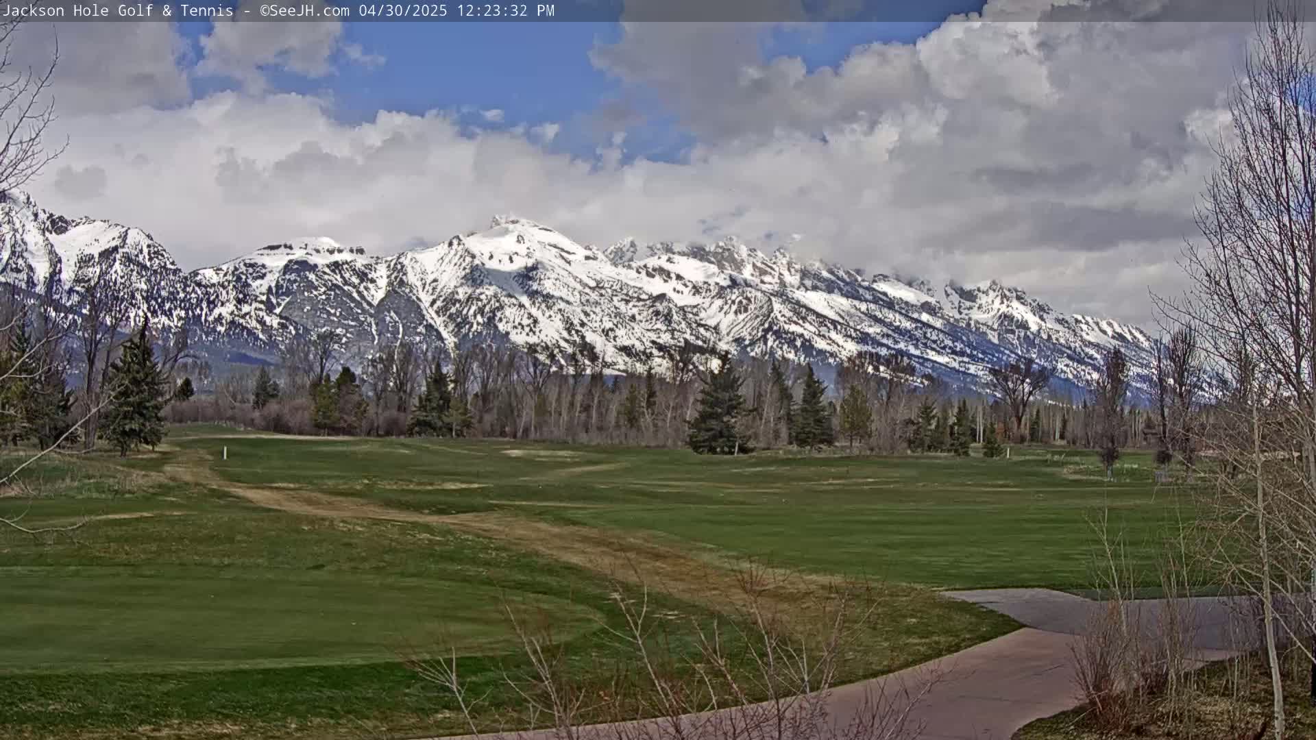 A partly cloudy day shows a snow-capped mountain range in the background of a green golf course.