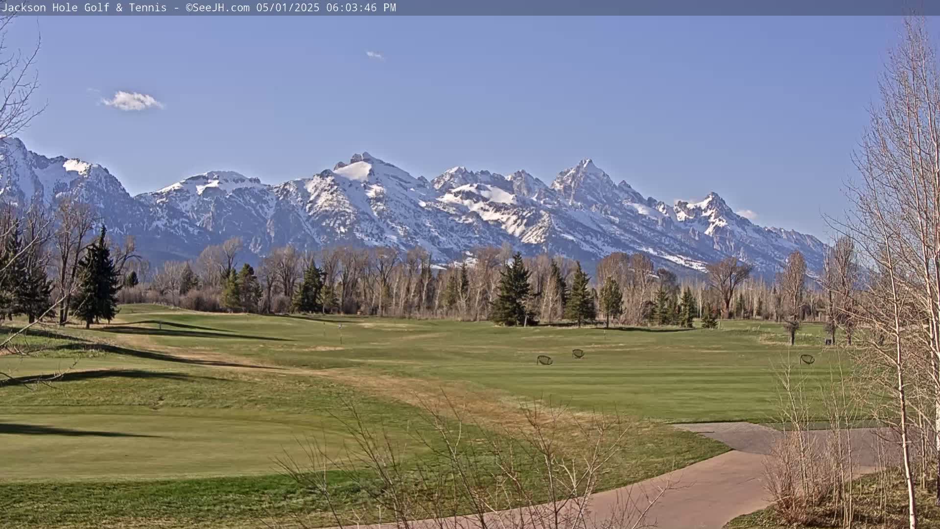 A snow-capped mountain range is visible in the background of a sunny golf course.