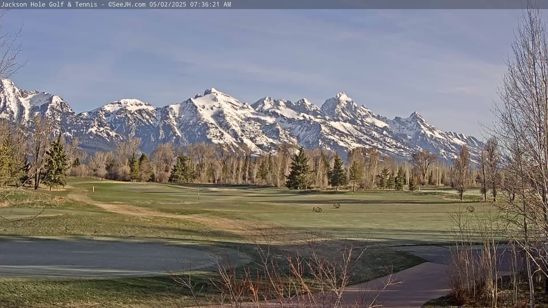 A snow-capped mountain range is visible in the background of a golf course on a sunny morning.