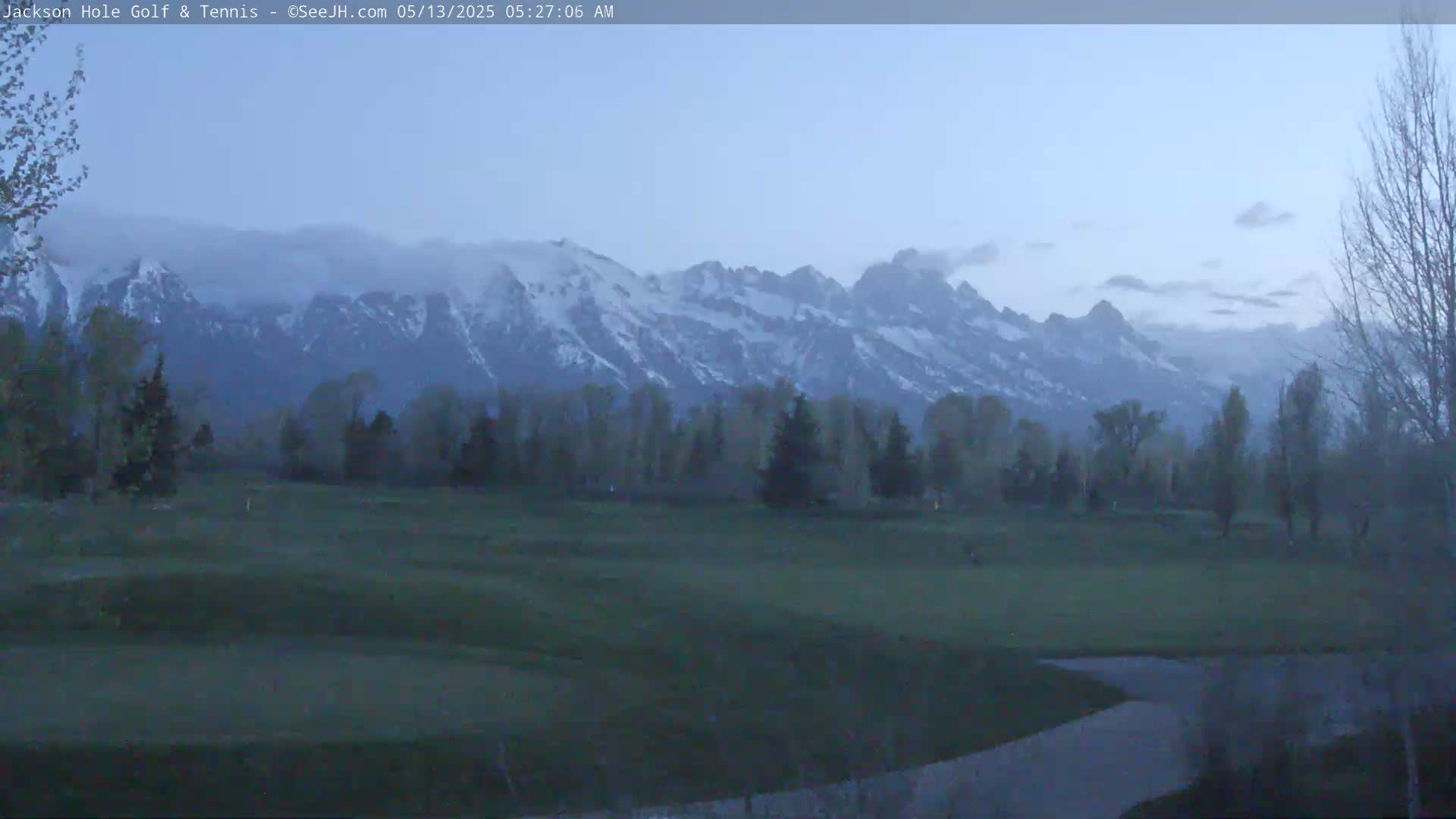 A golf course is visible in the foreground, with snow-capped mountains in the background under a hazy, twilight sky.