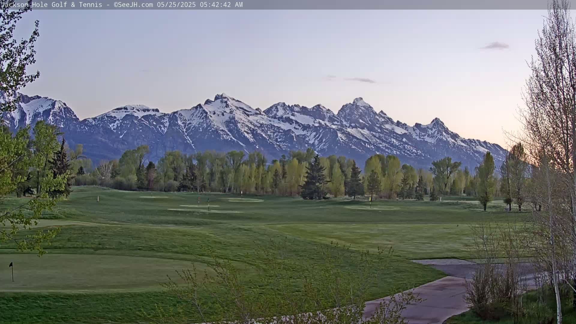 A snow-capped mountain range is visible in the distance behind a green golf course on a clear, early morning.