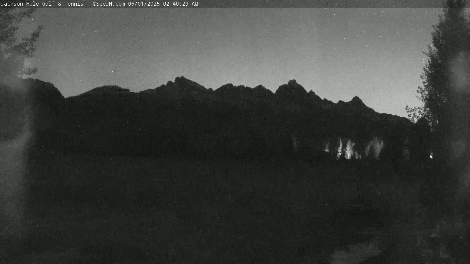 A dark, nighttime view shows a silhouetted mountain range under a mostly clear sky with a few visible stars.