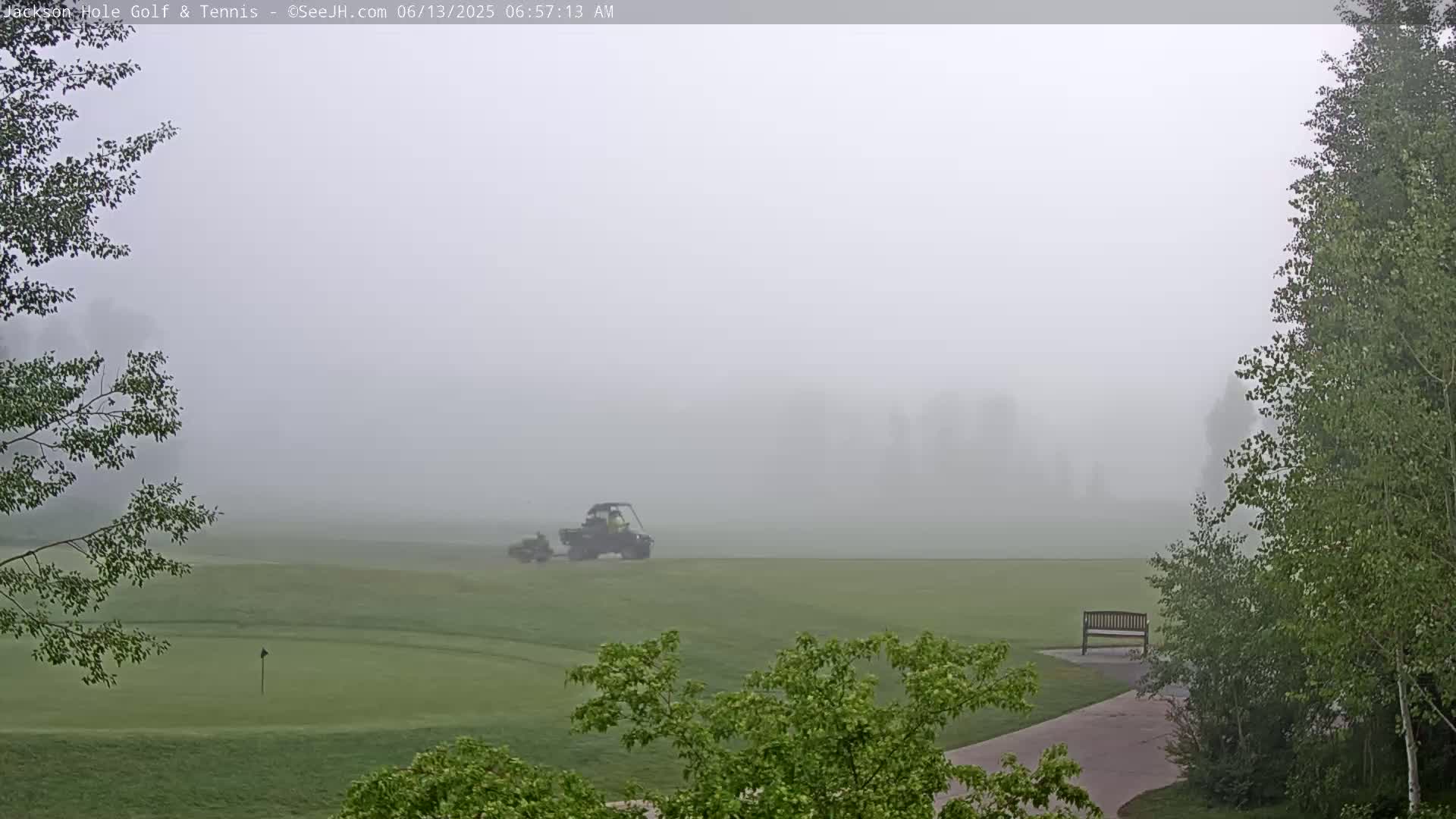 A golf course, shrouded in thick fog, features a small utility vehicle driving across a putting green.