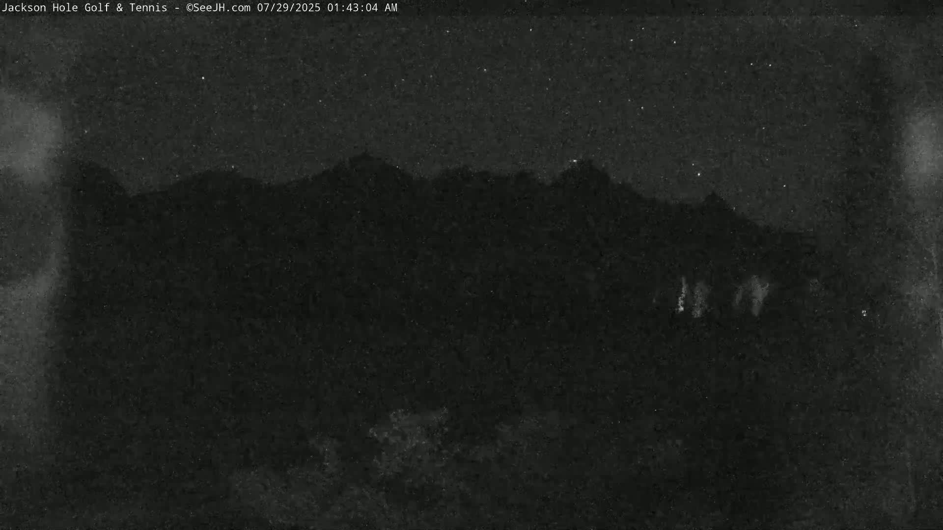 A nighttime, low-light view of a dark mountain range under a starry sky.