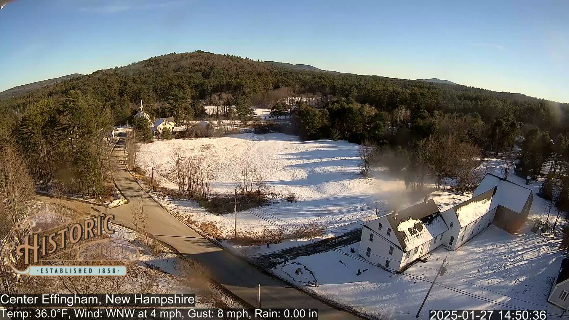 A snow-covered town nestled among wooded hills on a sunny day with a light wind.