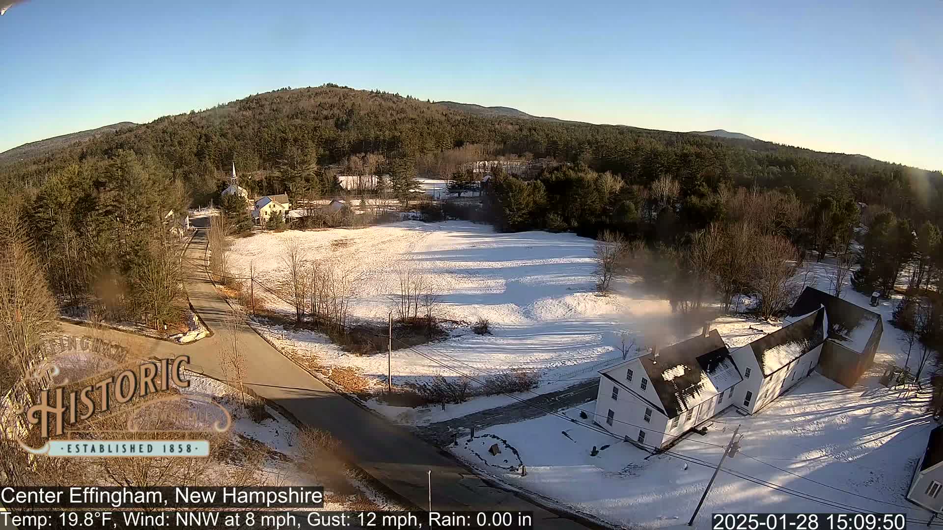 A snow-covered village scene with a road, houses, and trees under a clear, sunny sky.
