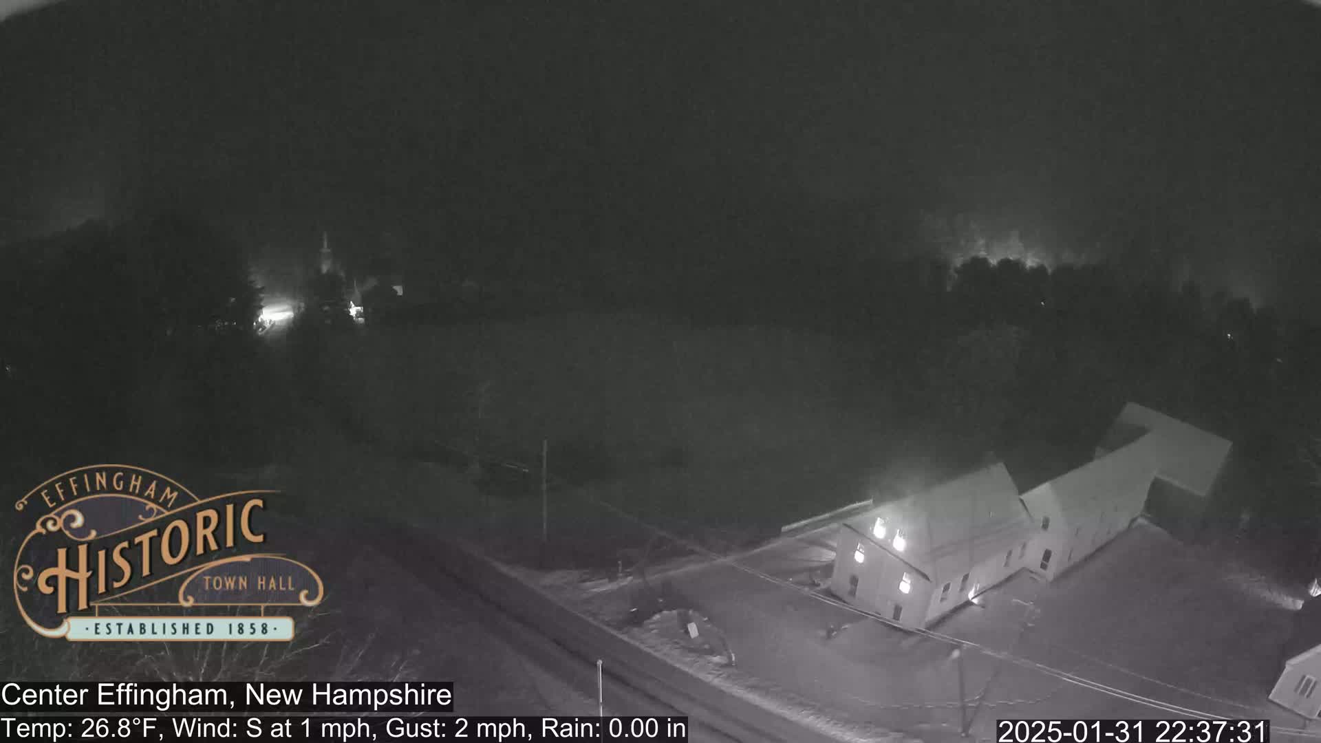 A nighttime aerial view of a building complex under a dark, rainy sky.