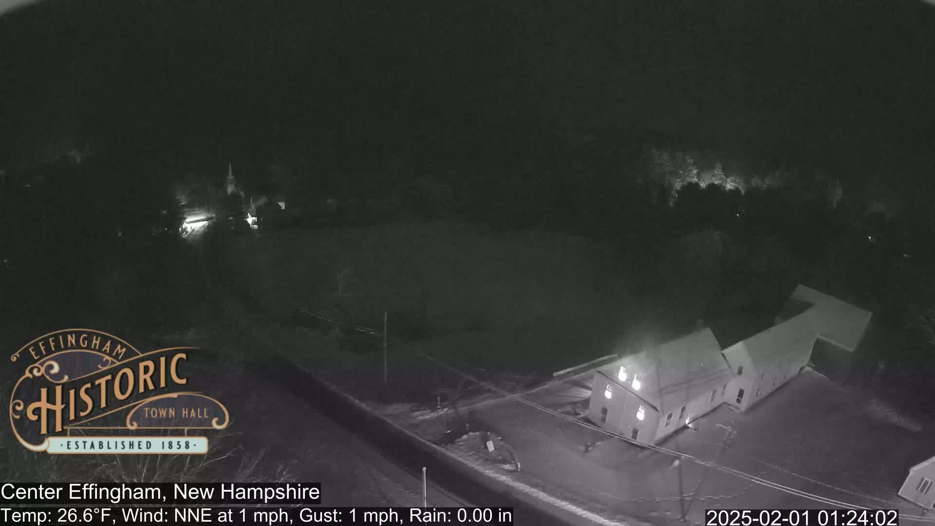 A nighttime, low-light aerial view of a building and surrounding area with calm wind and no rain.