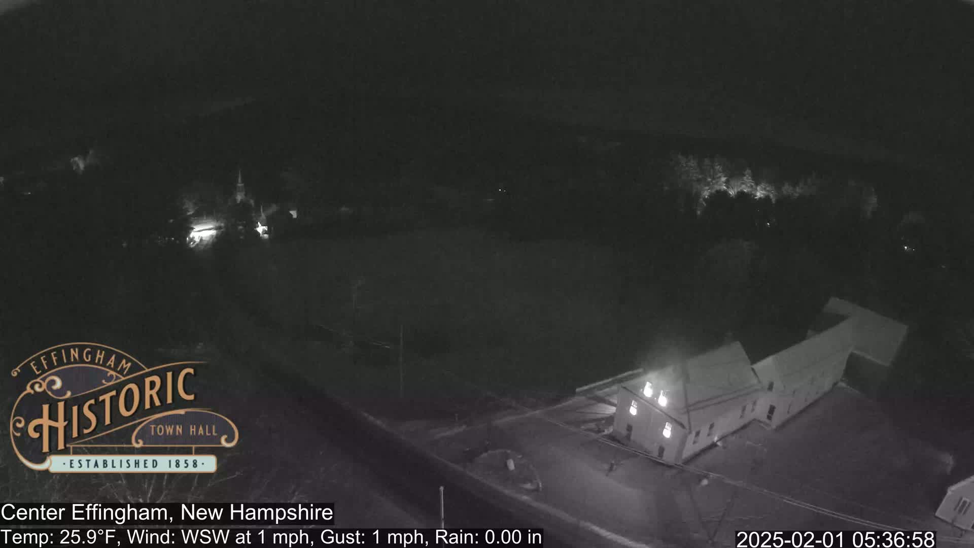A nighttime, low-light view of a building and surrounding area under rainy conditions with a temperature of 25.9°F and a light wind.