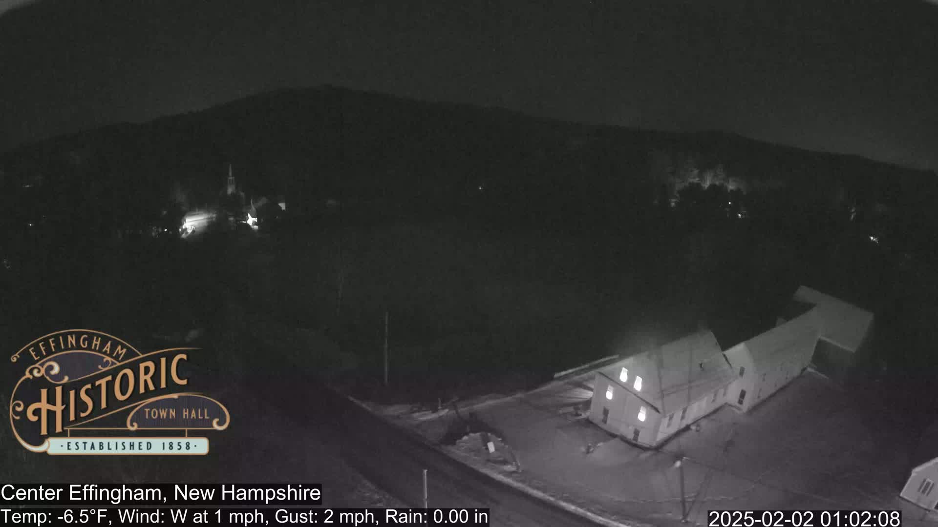 A nighttime, rainy view of a building and surrounding area, with a light dusting of snow on the ground.