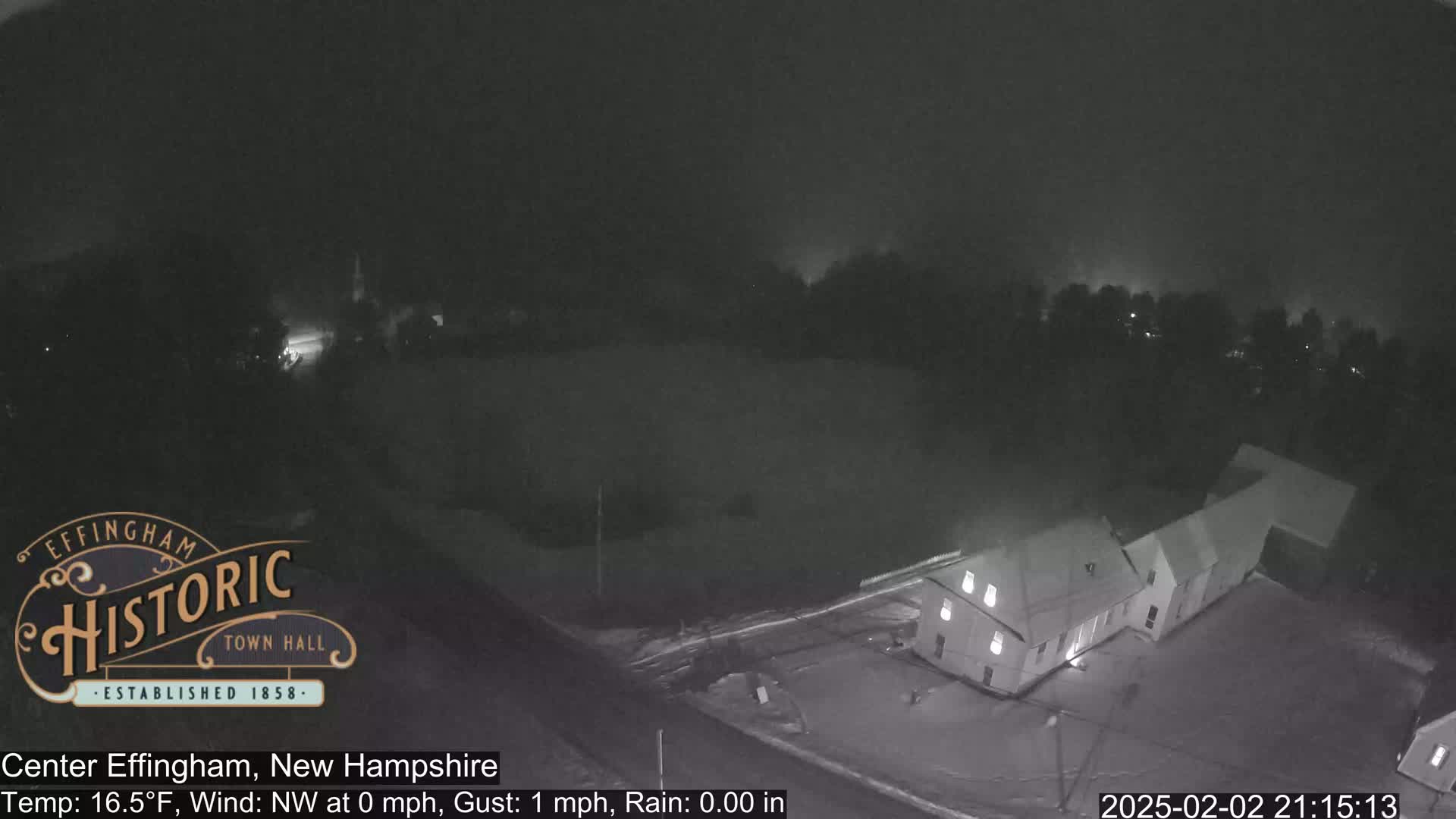 A nighttime, snow-covered scene shows a building and surrounding area under a dark, overcast sky.