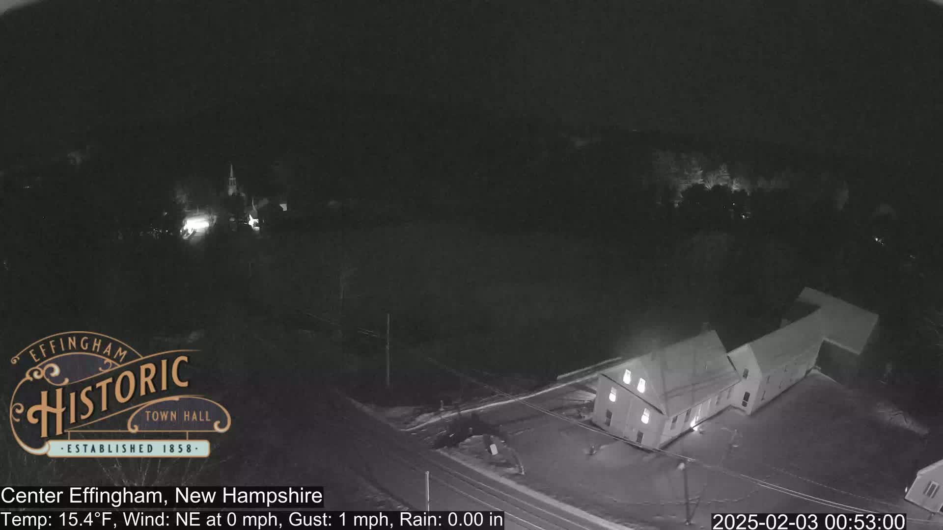 A nighttime, overhead view of a small town with a building illuminated, under calm conditions with no rain.