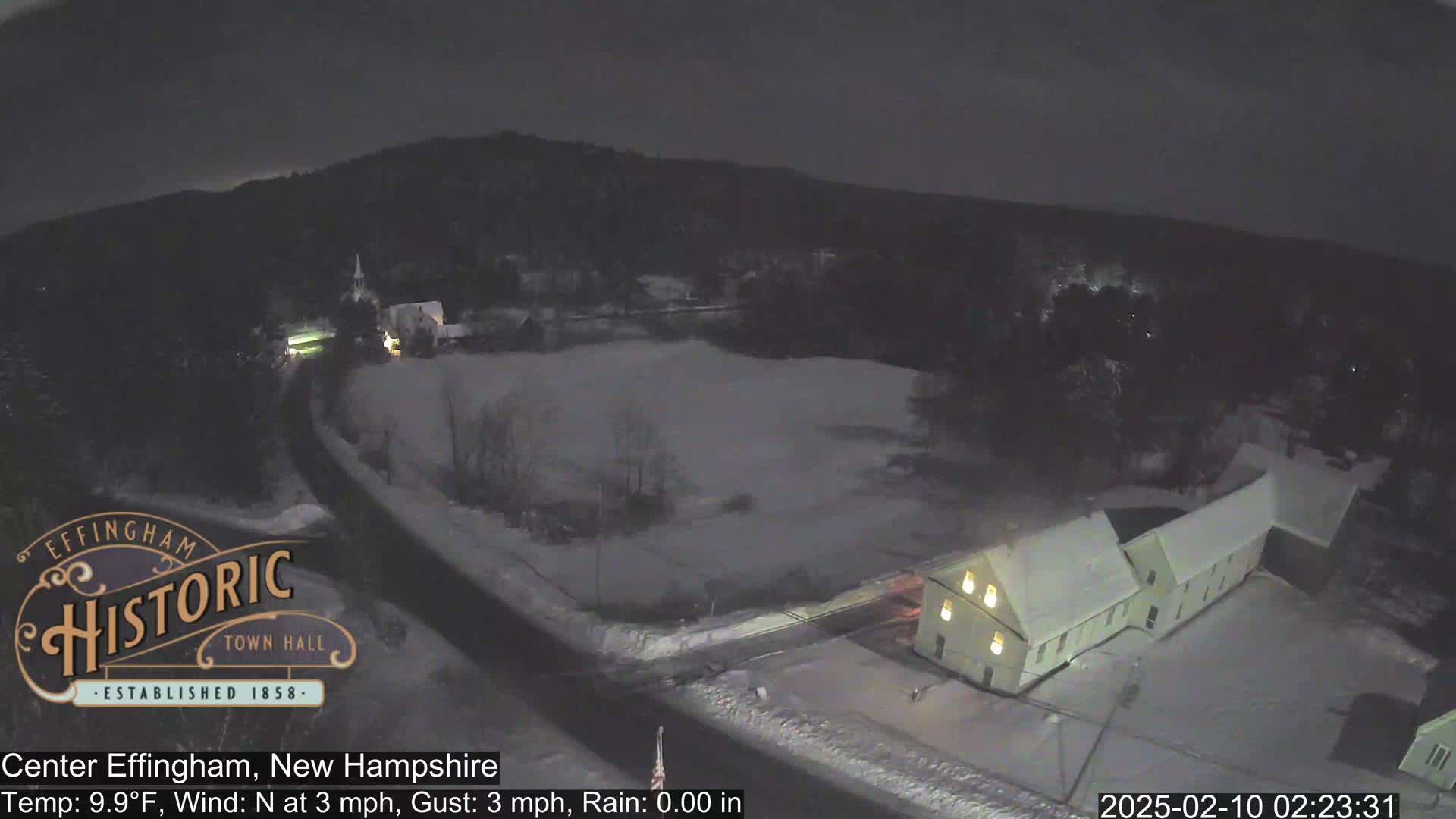A snow-covered town at night, with a building illuminated and a road visible.