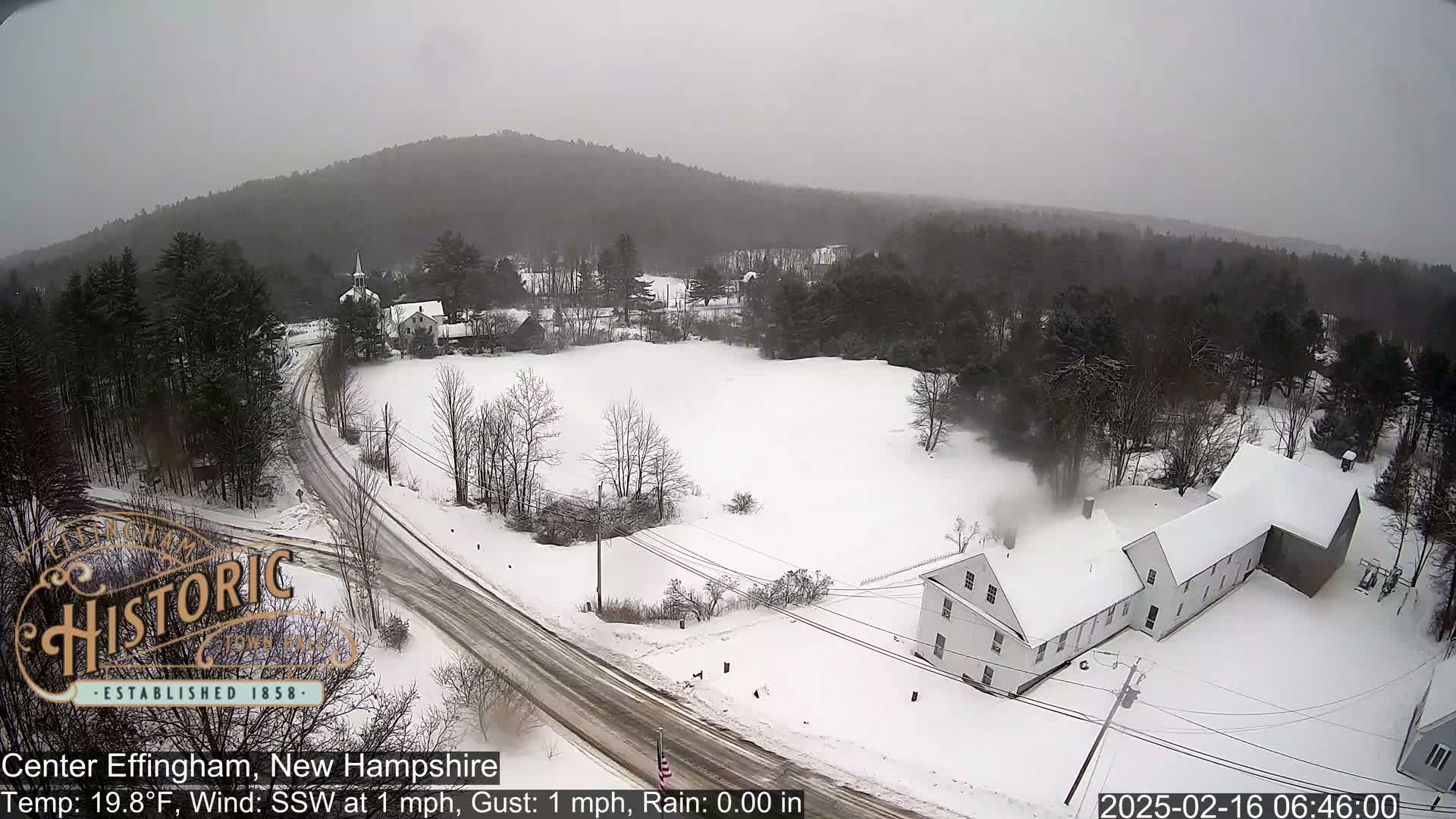 A snow-covered landscape with buildings and roads, under an overcast sky.