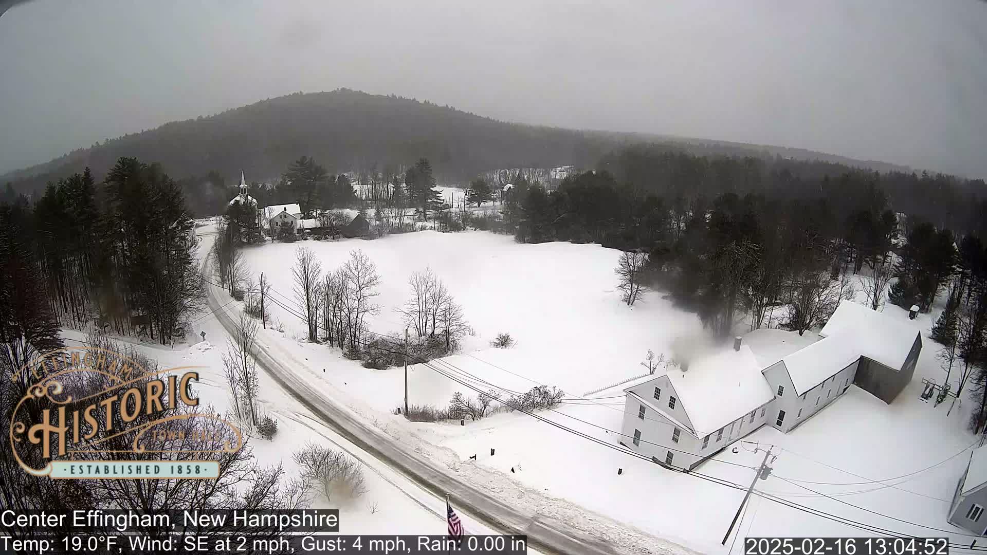 A snow-covered landscape with buildings and roads, under an overcast sky.