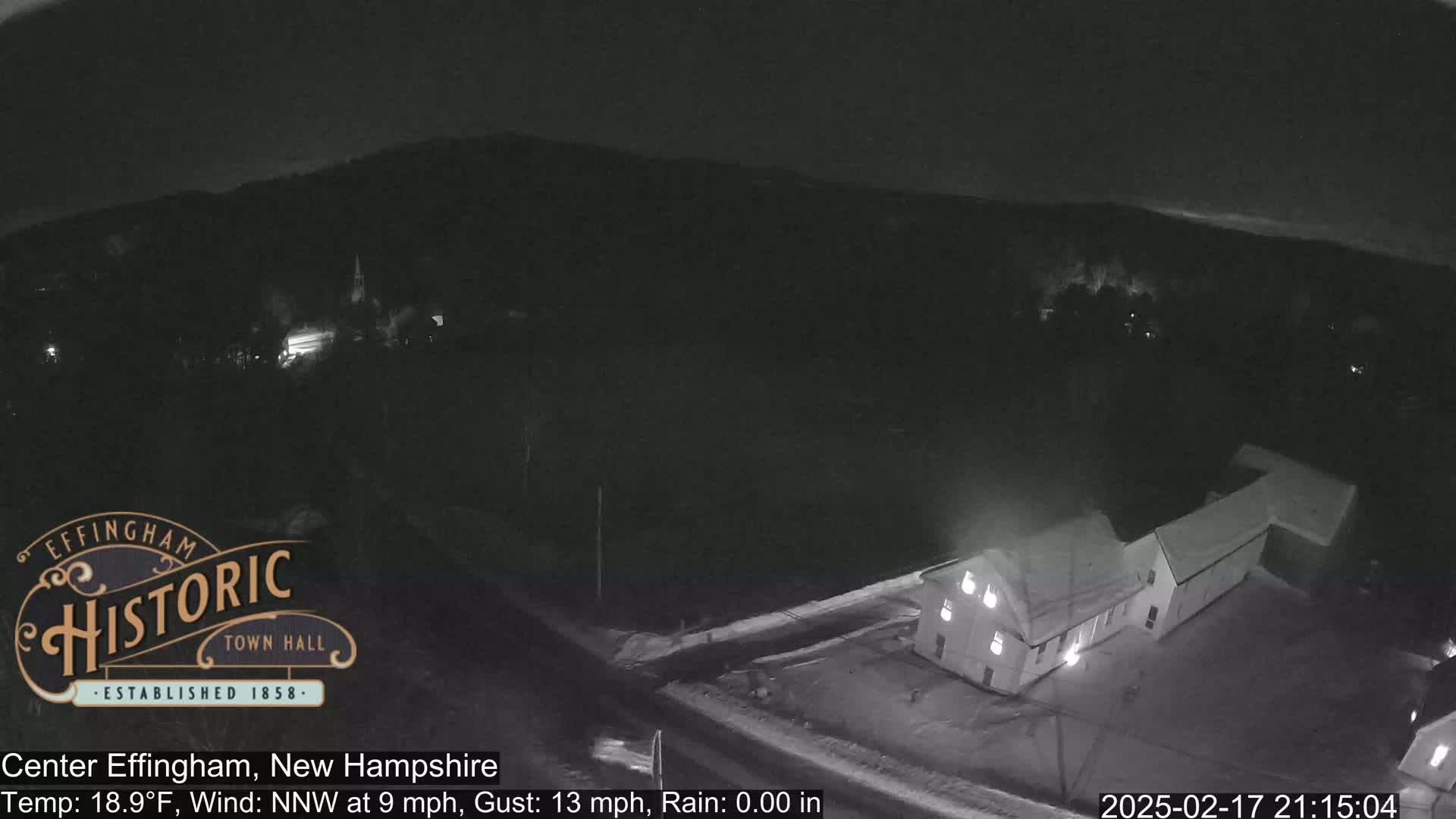 A nighttime, aerial view of a building in the rain, with a sparsely lit landscape visible in the background.