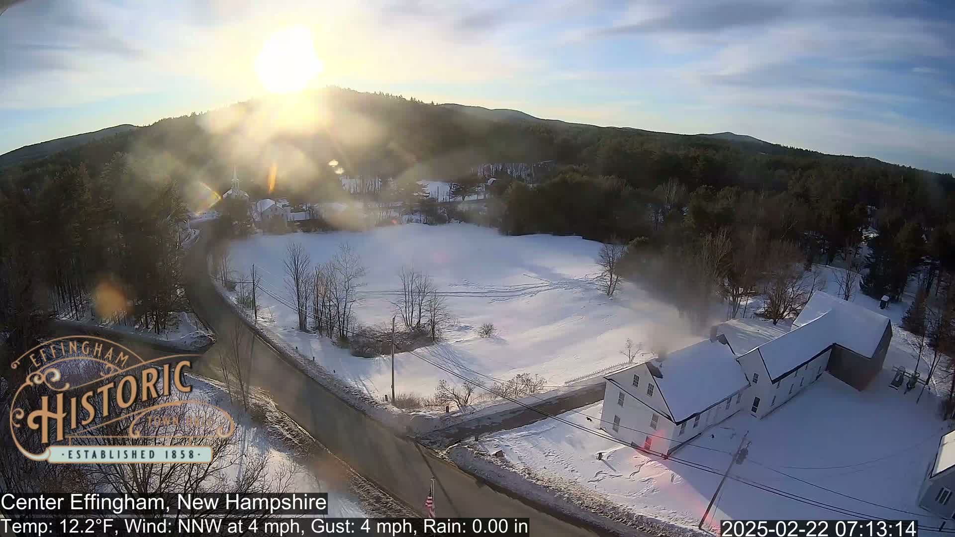 A snow-covered landscape with a white house and a road, under a bright, sunny sky.