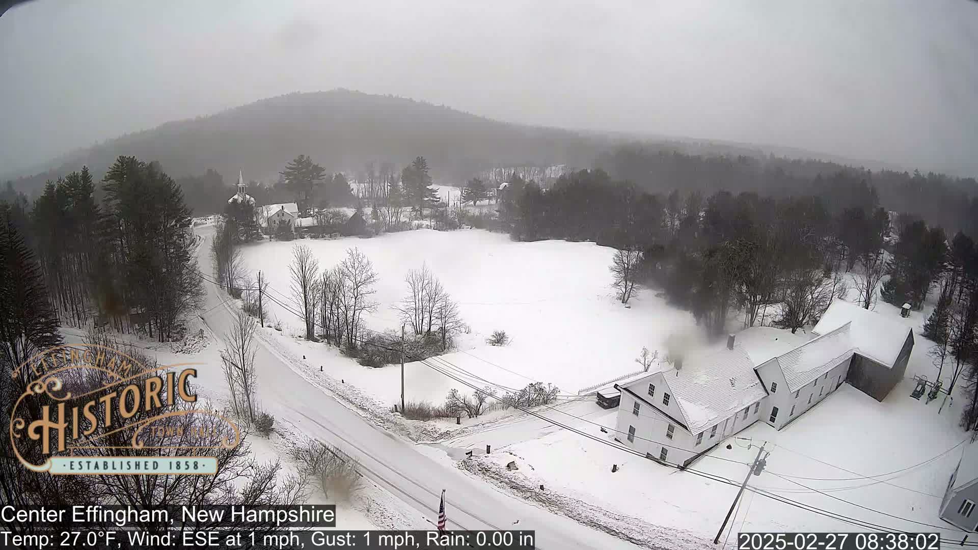 A snow-covered landscape with houses and trees under an overcast sky.