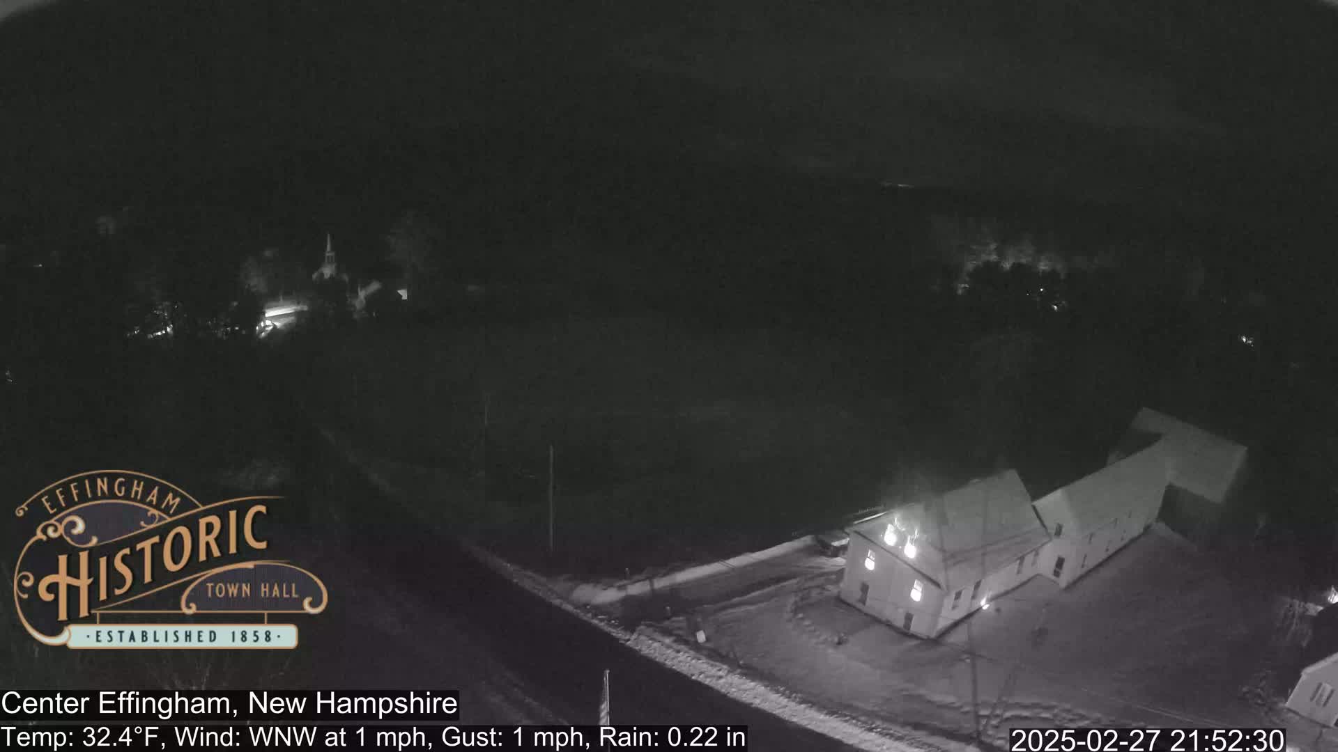 A nighttime, rainy view of a building complex with snow on the ground.