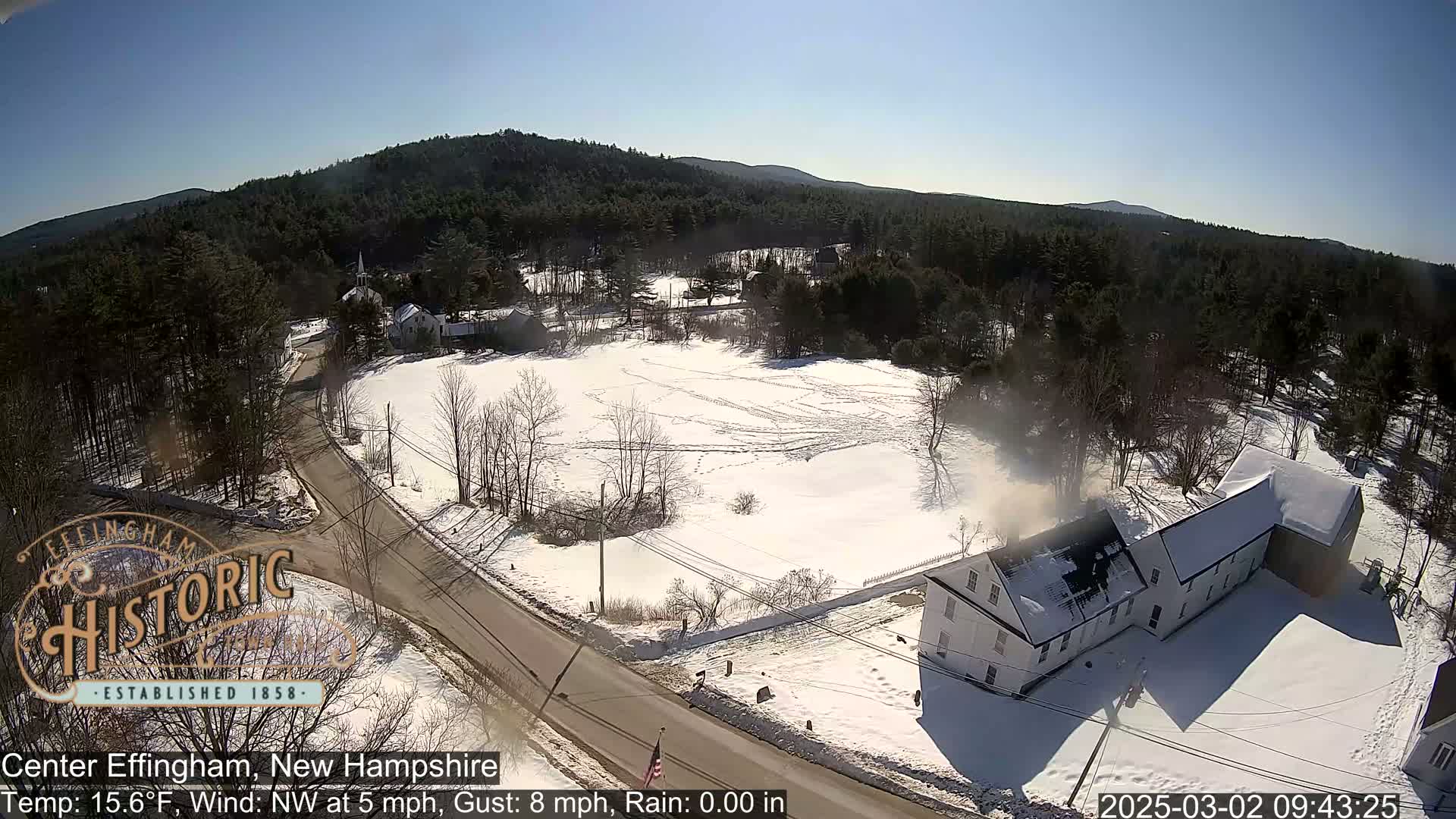 A snow-covered landscape with a long white building and a road, under a clear, sunny sky.